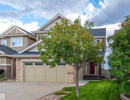 Two-story home with a tan siding exterior, stone facade accents, and a dark shingle roof - 1419 Chahley Place Nw, Edmonton, AB - Outdoor With Facade