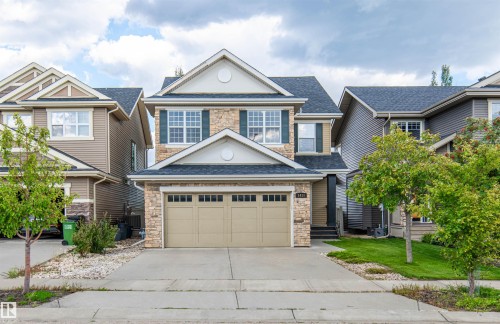 Stone and siding exterior with dark shutters, attached two-car garage, concrete driveway, and front lawn - 1419 Chahley Place Nw, Edmonton, AB - Outdoor With Facade