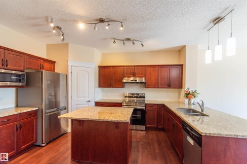 Kitchen featuring wood-finish flooring, wood cabinetry, stainless steel appliances, granite countertops, and an island - 1419 Chahley Place Nw, Edmonton, AB - Indoor Photo Showing Kitchen With Stainless Steel Kitchen With Double Sink