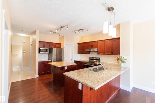 Kitchen featuring wood-finish flooring, two islands with stone countertops, stainless steel appliances, and track lighting - 1419 Chahley Place Nw, Edmonton, AB - Indoor Photo Showing Kitchen With Stainless Steel Kitchen With Double Sink