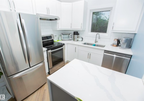 Contemporary kitchen featuring white cabinetry, stainless steel appliances including a refrigerator, range, and dishwasher, a white subway tile backsplash, and a white countertop with subtle gray veining - 11131 52 Street Nw, Edmonton, AB - Indoor Photo Showing Kitchen With Upgraded Kitchen