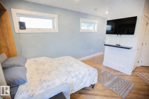 Wood-finish flooring throughout this room featuring a mounted flat-screen television with a floating shelf below - 11131 52 Street Nw, Edmonton, AB - Indoor Photo Showing Bedroom