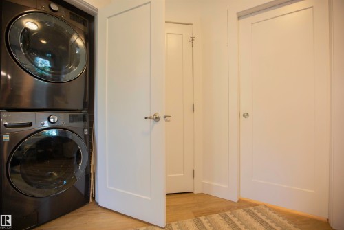 Stackable washer and dryer unit with modern panel doors and wood-finish flooring - 11131 52 Street Nw, Edmonton, AB - Indoor Photo Showing Laundry Room