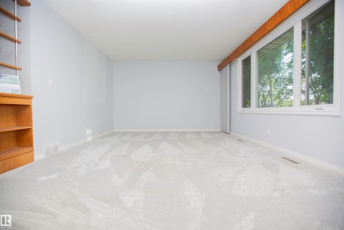 Spacious room featuring light gray walls, plush patterned carpeting, and a large multi-pane window with wood trim - 11131 52 Street Nw, Edmonton, AB - Indoor Photo Showing Other Room