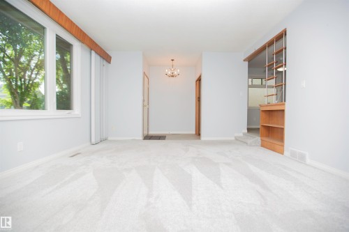 Carpeted living area featuring light gray walls, large windows with white trim, and a built-in wooden shelving unit - 11131 52 Street Nw, Edmonton, AB - Indoor Photo Showing Other Room