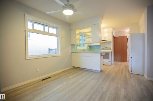 Open-concept kitchen and dining area featuring light wood-finish flooring, a white ceiling fan with integrated lighting, and a large window with white trim - 11131 52 Street Nw, Edmonton, AB - Indoor