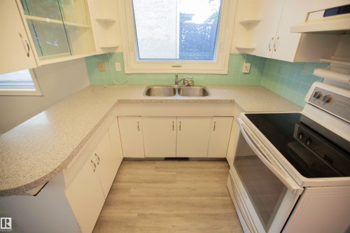 U-shaped kitchen featuring white cabinetry, light-colored countertops, and a double-basin stainless steel sink with a window above - 11131 52 Street Nw, Edmonton, AB - Indoor Photo Showing Kitchen
