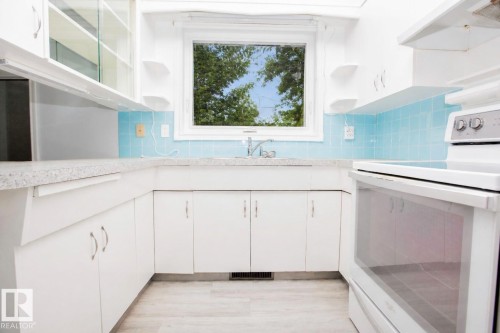 Kitchen featuring a window above the sink, light blue subway tile backsplash, white cabinetry, light-colored countertops, and wood-finish flooring - 11131 52 Street Nw, Edmonton, AB - Indoor