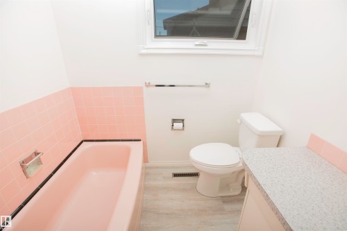 Bathroom featuring a pink bathtub, matching wall tile, and light-tone wood-finish flooring - 11131 52 Street Nw, Edmonton, AB - Indoor Photo Showing Bathroom