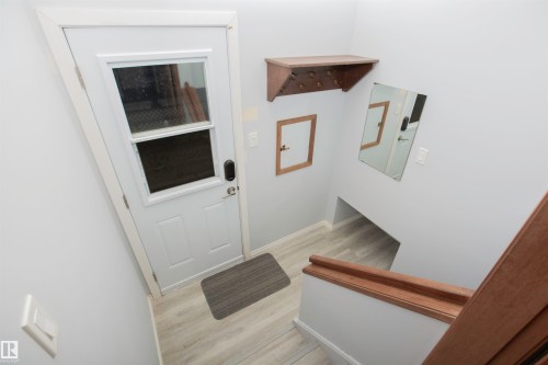 Entryway with light wood-finish flooring, white paneled door with upper glass panel, and contrasting wood staircase - 11131 52 Street Nw, Edmonton, AB - Indoor Photo Showing Other Room