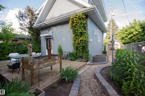 Side exterior featuring light grey siding with white trim, a wood deck, a gravel pathway with paver edging, mature perimeter greenery, and a detached storage shed - 11131 52 Street Nw, Edmonton, AB - Outdoor With Exterior