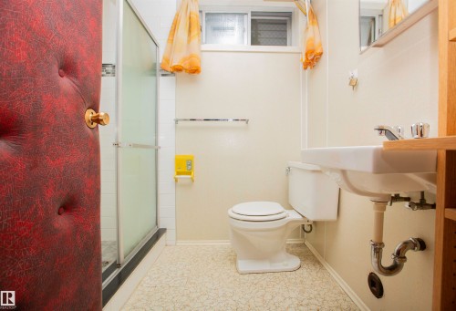 Bathroom featuring a white toilet, wall-mounted sink, and a shower enclosure with frosted glass panels - 11131 52 Street Nw, Edmonton, AB - Indoor Photo Showing Bathroom