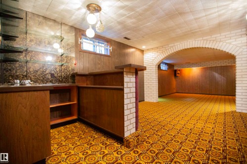 Finished basement with an arched brick entryway, wood-paneled walls, and a built-in bar featuring glass shelving and a patterned accent wall - 11131 52 Street Nw, Edmonton, AB - Indoor Photo Showing Other Room