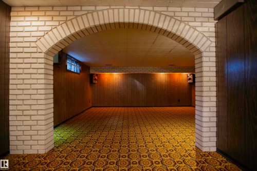 Arched brick doorway opening to a room featuring patterned carpet, wood-paneled walls, and a recessed window - 11131 52 Street Nw, Edmonton, AB - Indoor Photo Showing Other Room