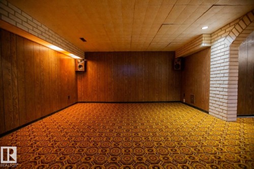 Spacious room featuring wood paneling, white brick accents, and patterned carpet flooring - 11131 52 Street Nw, Edmonton, AB - Indoor Photo Showing Other Room
