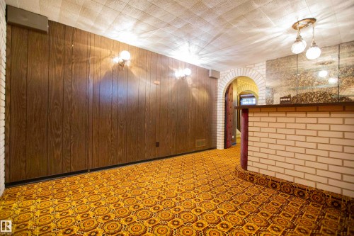 Entertainment space featuring wood-finish wall paneling, patterned carpet, and a built-in brick bar with mirrored backsplash - 11131 52 Street Nw, Edmonton, AB - Indoor Photo Showing Other Room