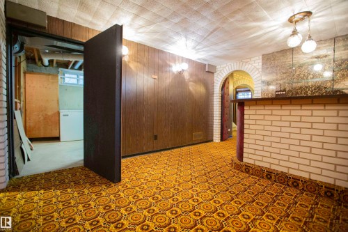 Recreational space featuring patterned carpet flooring, wood-panel walls, and a built-in bar with light brick detailing and a dark countertop - 11131 52 Street Nw, Edmonton, AB - Indoor Photo Showing Other Room