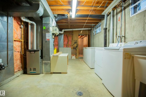 Utility area featuring concrete flooring, exposed ceiling joists, multiple laundry appliances, and a visible furnace unit - 11131 52 Street Nw, Edmonton, AB - Indoor Photo Showing Laundry Room