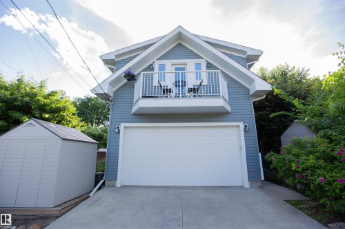 Detached structure featuring blue horizontal siding, white trim, a single overhead garage door, a second-story balcony with white railings, and a concrete driveway - 11131 52 Street Nw, Edmonton, AB - Outdoor