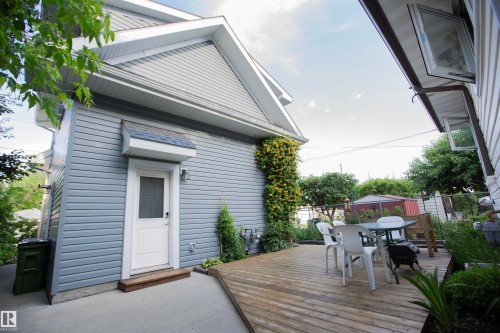 Expansive wood-finish deck bordered by a perennial garden, offering direct access to the property via a white entrance door with a protective awning - 11131 52 Street Nw, Edmonton, AB - Outdoor With Exterior