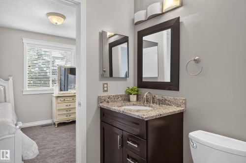 Bathroom featuring a dark wood-finish vanity with a stone countertop, an undermount sink with a brushed nickel faucet, and a wall-mounted mirror - 12724 148 Avenue Nw, Edmonton, AB - Indoor Photo Showing Bathroom