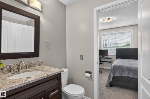 Bathroom vanity with a dark wood-finish cabinet and a light-toned stone countertop, featuring an undermount sink and a brushed nickel faucet - 12724 148 Avenue Nw, Edmonton, AB - Indoor Photo Showing Bathroom