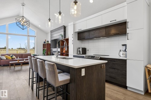 Open-concept kitchen featuring a large island with a countertop, wood-finish flooring, white cabinetry, dark wood-finish cabinetry, and stainless steel appliances - 45 Evermore Crescent, St. Albert, AB - Indoor Photo Showing Kitchen With Upgraded Kitchen