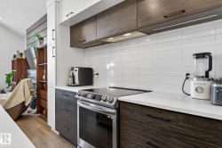 Stainless steel range with a smooth cooktop, white subway tile backsplash, white countertops, dark wood-finish lower cabinetry, and contrasting white and dark wood-finish upper cabinetry - 