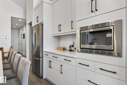 White cabinetry with matte black hardware, stainless steel refrigerator, built-in stainless steel microwave, white countertop, and white subway tile backsplash - 45 Evermore Crescent, St. Albert, AB - Indoor Photo Showing Kitchen