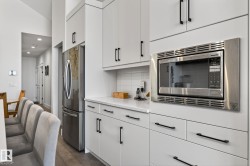 White cabinetry with matte black hardware, stainless steel refrigerator, built-in stainless steel microwave, white countertop, and white subway tile backsplash - 