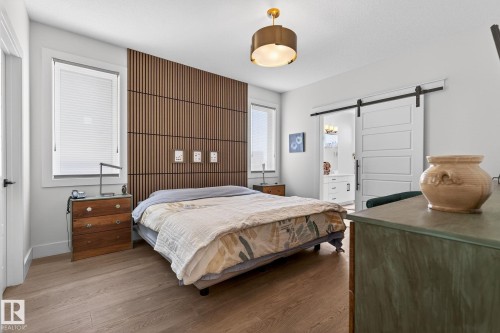 Wood-finish flooring, accent wall with vertical wood paneling, contemporary flush mount lighting, sliding barn door, and white window blinds - 45 Evermore Crescent, St. Albert, AB - Indoor Photo Showing Bedroom