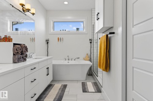 Dual-sink vanity with white cabinetry and matte black hardware, freestanding bathtub, walk-in shower with tiled walls, and white wall-mounted storage cabinet - 45 Evermore Crescent, St. Albert, AB - Indoor Photo Showing Bathroom