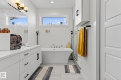 Dual-sink vanity with white cabinetry and matte black hardware, freestanding bathtub, walk-in shower with tiled walls, and white wall-mounted storage cabinet - 