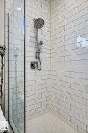 Enclosed shower with subway tile walls, a rain shower head, hand-held shower, and herringbone pattern floor tiling - 