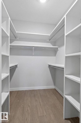 Walk-in closet featuring built-in shelving, multiple hanging rods, and wood-finish flooring - 45 Evermore Crescent, St. Albert, AB - Indoor With Storage