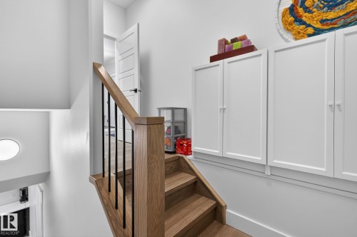 Wood-finish staircase with black metal balusters, leading to a landing with built-in white cabinetry - 45 Evermore Crescent, St. Albert, AB - Indoor Photo Showing Other Room