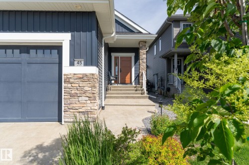 Contemporary exterior with vertical siding, stone accent detailing, a panel garage door, and a concrete pathway leading to the entry - 45 Evermore Crescent, St. Albert, AB - Outdoor With Facade