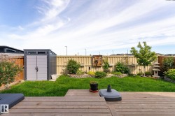 Expansive backyard featuring a wood deck, green lawn, garden beds with stone retaining walls, and a storage shed - 