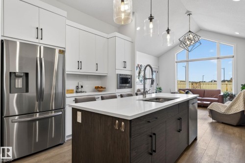Vaulted ceilings with abundant natural light, stainless steel appliances, white cabinetry, a large kitchen island with seating, and wood-finish flooring - 45 Evermore Crescent, St. Albert, AB - Indoor Photo Showing Kitchen With Stainless Steel Kitchen With Double Sink With Upgraded Kitchen