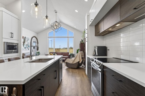 Modern kitchen featuring an expansive island with a double basin sink, white countertops, dark wood-finish cabinetry, and stainless steel appliances - 45 Evermore Crescent, St. Albert, AB - Indoor Photo Showing Kitchen With Double Sink With Upgraded Kitchen