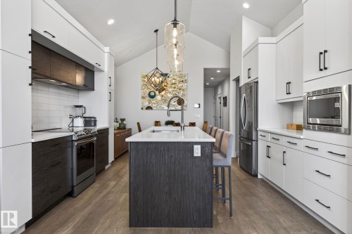 Vaulted ceiling kitchen featuring an island with counter seating, stainless steel appliances, white subway tile backsplash, and wood-finish flooring - 45 Evermore Crescent, St. Albert, AB - Indoor Photo Showing Kitchen With Stainless Steel Kitchen With Upgraded Kitchen