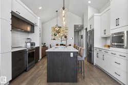 Vaulted ceiling kitchen featuring an island with counter seating, stainless steel appliances, white subway tile backsplash, and wood-finish flooring - 