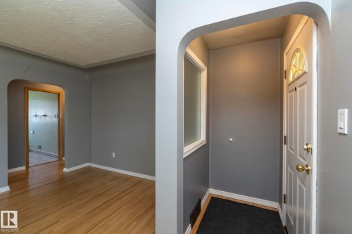 Wood-finish flooring, arched doorways, a white paneled entry door with decorative glass, and a frosted fixed window - 12322 94 Street Nw, Edmonton, AB - Indoor Photo Showing Other Room