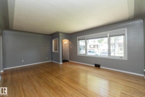 Hardwood flooring throughout, multiple windows with roller shades, and a white paneled entry door with an arched transom - 12322 94 Street Nw, Edmonton, AB - Indoor Photo Showing Other Room