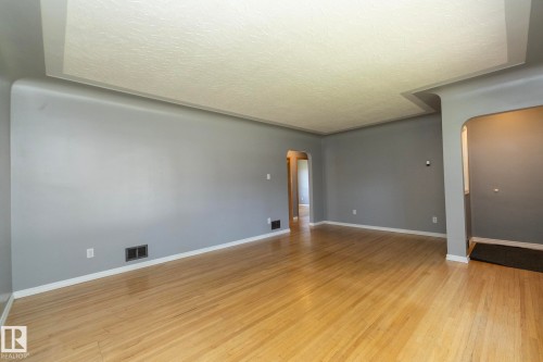 Spacious living area showcasing warm wood-finish flooring, fresh gray painted walls, recessed ceiling lighting, and multiple windows providing natural illumination throughout the room - 12322 94 Street Nw, Edmonton, AB - Indoor Photo Showing Other Room