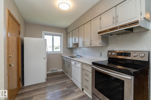 Kitchen featuring wood-finish flooring, white cabinetry, a white countertop, a tile backsplash, and stainless steel appliances - 12322 94 Street Nw, Edmonton, AB - Indoor Photo Showing Kitchen With Double Sink