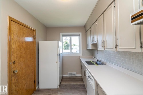 Wood-finish flooring with white baseboards, kitchen features white cabinetry with metal pulls, stainless steel sink with dual faucets, and a light-colored countertop - 12322 94 Street Nw, Edmonton, AB - Indoor Photo Showing Kitchen
