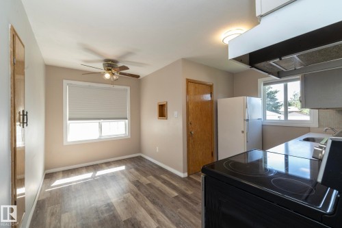 Wood-finish flooring throughout, bright window with blinds, ceiling fan with integrated lighting, kitchen featuring range hood and electric range - 12322 94 Street Nw, Edmonton, AB - Indoor