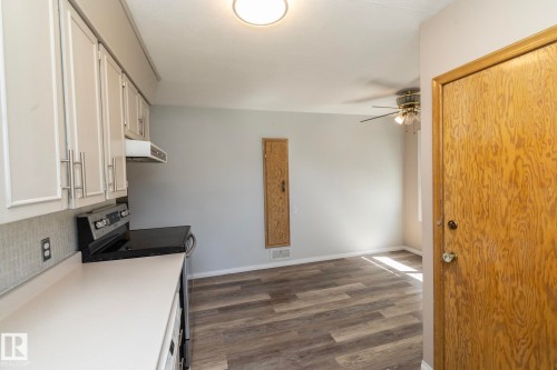 White cabinetry with brushed nickel hardware, stainless steel range with overhead ventilation, light-toned countertop, wood-finish flooring, and ceiling fan - 12322 94 Street Nw, Edmonton, AB - Indoor