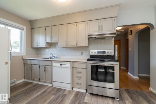 Bright kitchen featuring cream cabinetry, stainless steel appliances including a convection oven and dishwasher, white subway tile backsplash, and wood-finish flooring throughout - 12322 94 Street Nw, Edmonton, AB - Indoor Photo Showing Kitchen
